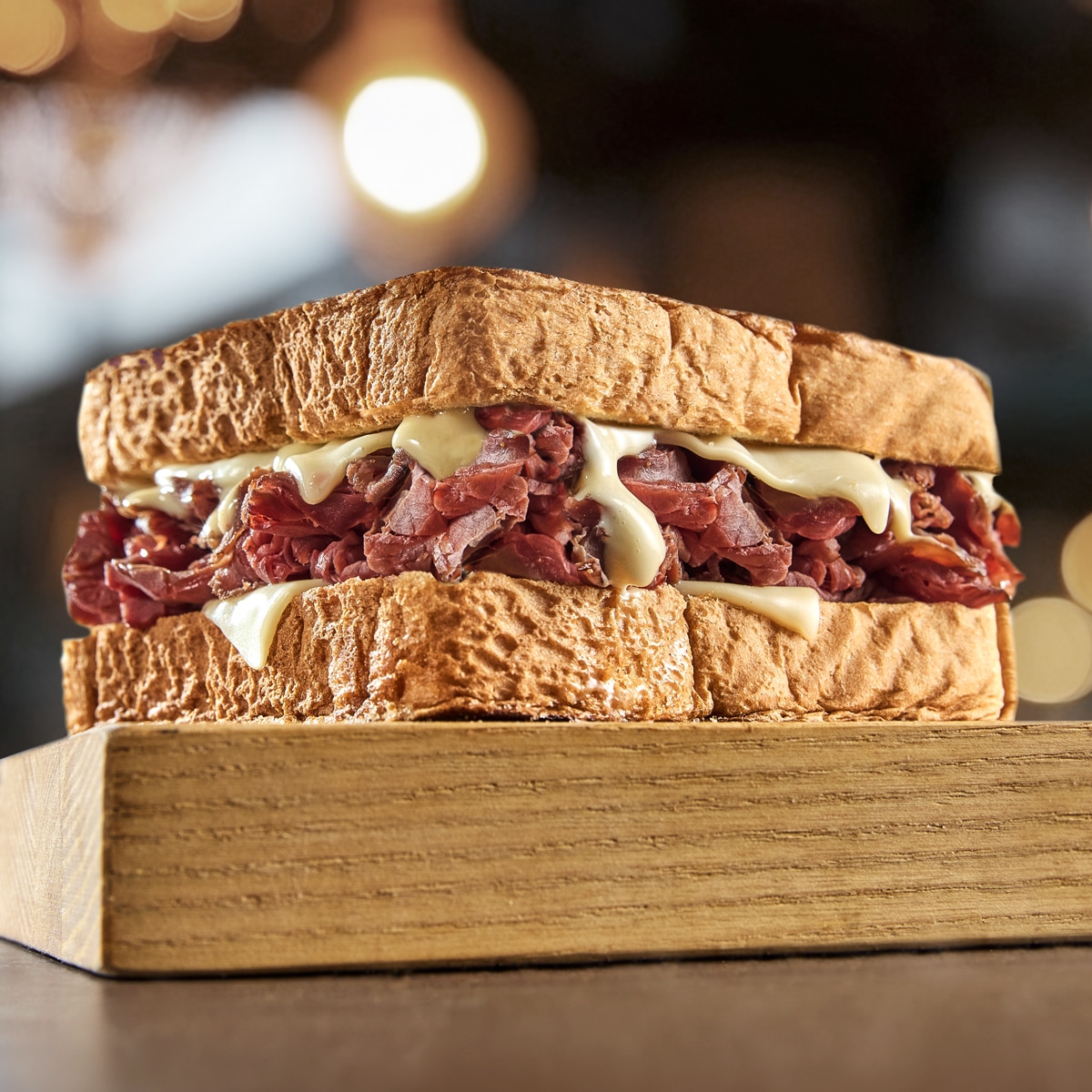 A photograph of a sandwich with thick bread, meat, and cheese. The sandwich is sitting on a wood cutting board.