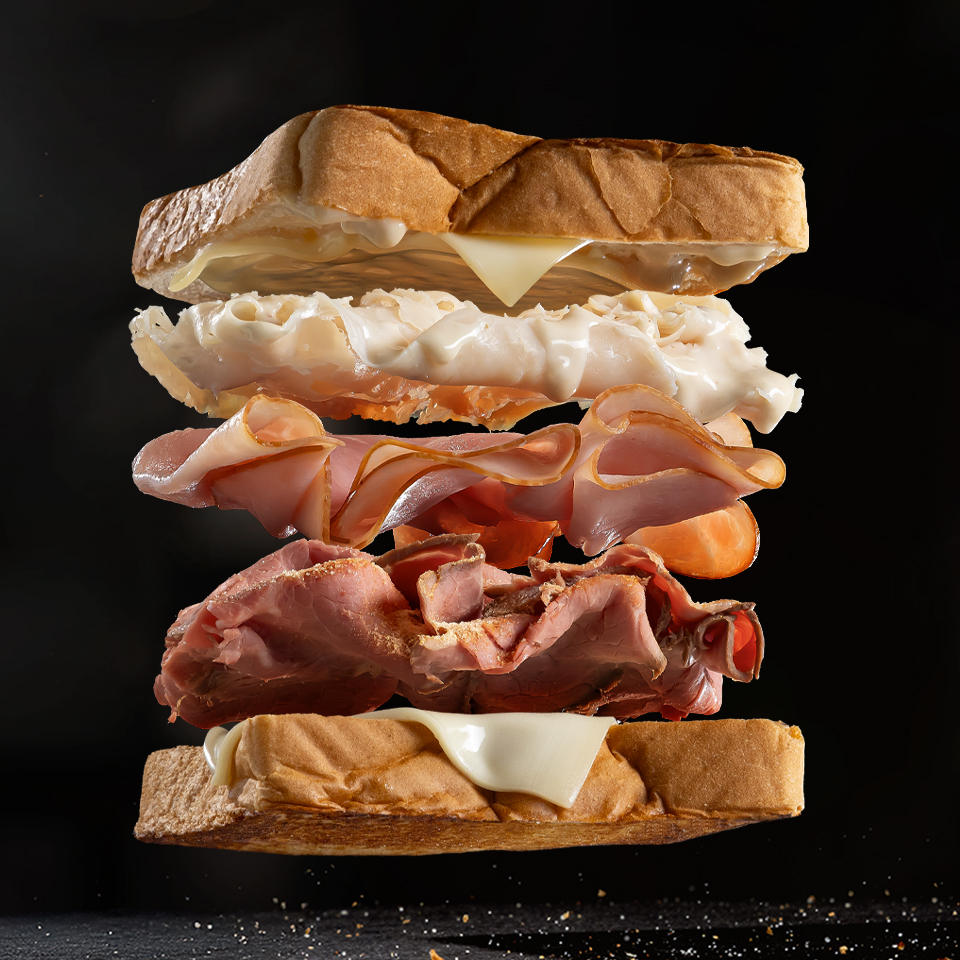 An image of a sandwich floating in the air which each layer separated between the bread, meats, cheeses. All on a black background